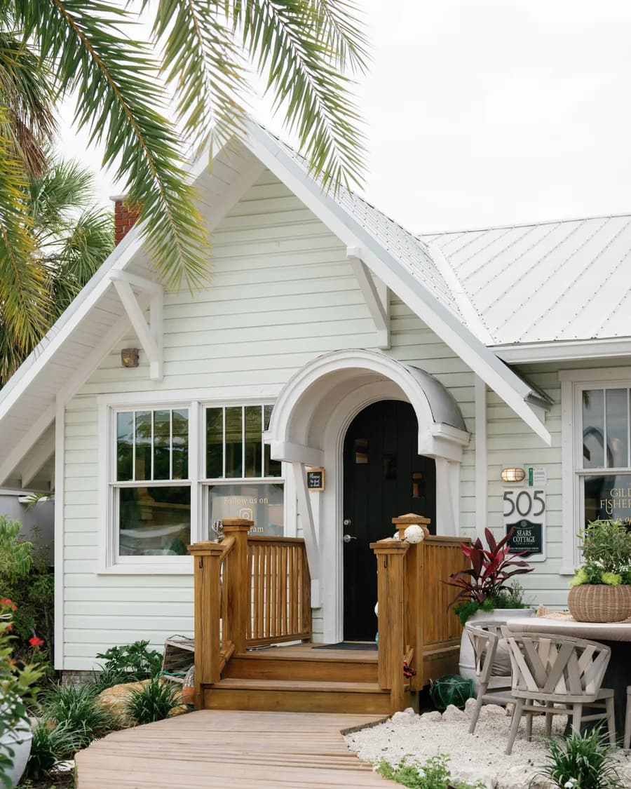The shop's front porch: an arched black door under a gabled portico, the number 505, framed by palms and a white picket fence