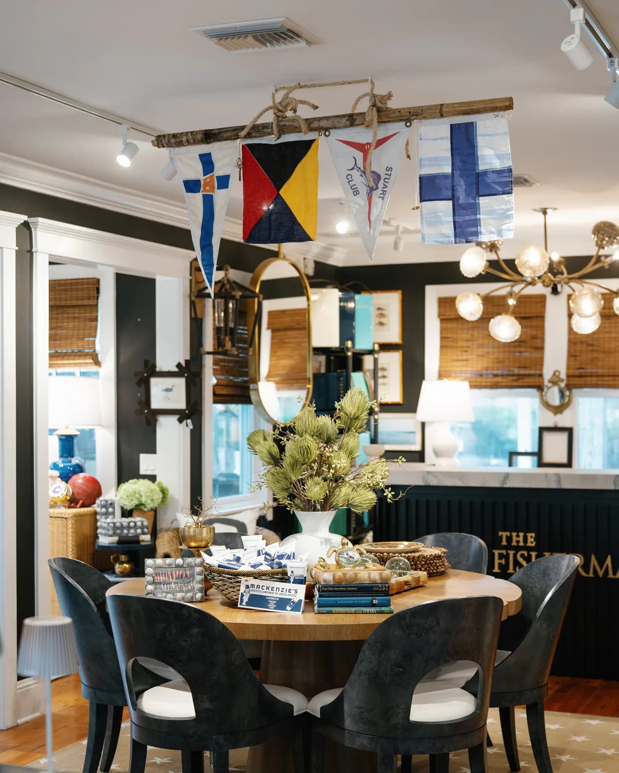 Inside the shop: a round table set beneath a string of nautical signal flags, dark chairs on a star-patterned rug, the marble counter and 'The Fisherman' sign beyond